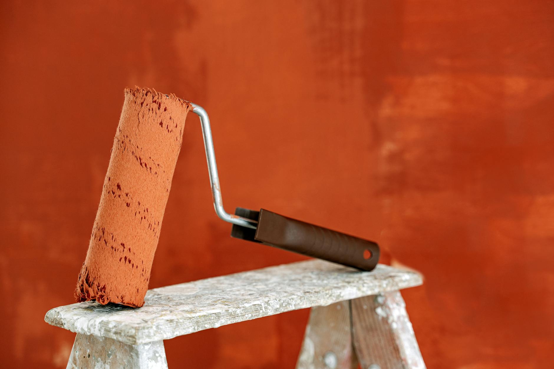 pexels-photo-5799051 - IFixSht Detailed image of a paint roller resting on a ladder with a vibrant orange wall in the background.